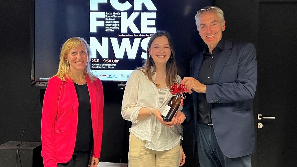 Heike Parakenings (DJV Hessen), Gewinnerin Caroline Rauch und Prof. Rüdiger Pichler stehen vor einem Plakat mit den Worten "FCK FKE NWS"
