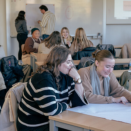 Studierende sitzen in einem Vorlesungssaal und arbeiten an einem großen Plakat
