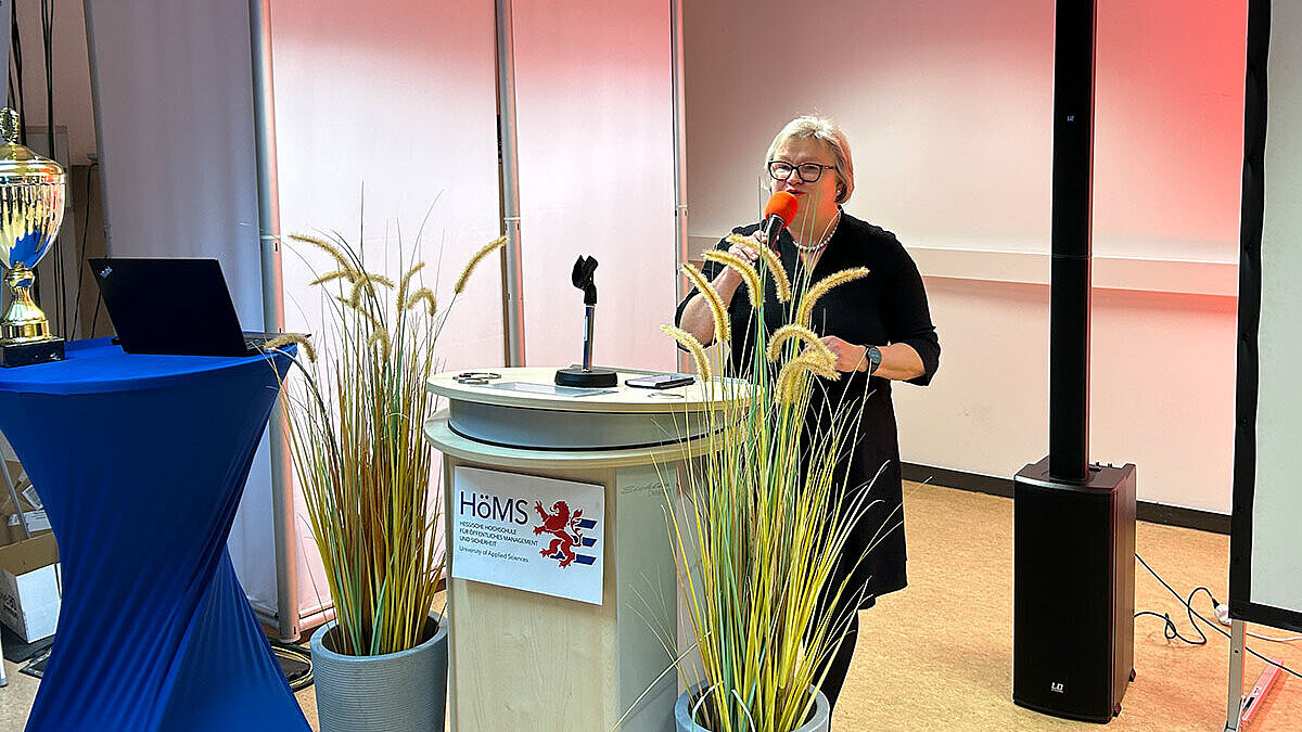 Prof. Dr. Eva Waller, Präsidentin der Hochschule RheinMain, steht mit einem Mikrofon in der Hand an einem Rednerpult und spricht zu den Gästen der Veranstaltung.