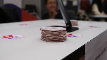 Ein Tisch mit einem Stapel runder, gestapelter Karten im Vordergrund. Auf dem Tisch sind mehrere Aufkleber mit einem Symbol sichtbar. Im Hintergrund ist unscharf eine Person zu erkennen.