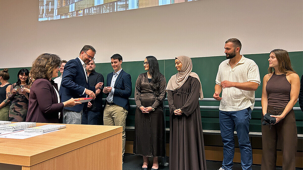 Absolvent:innen der Hochschule RheinMain stehen in einer Reihe und erhalten nacheinander ein Präsent aus den Händen der Vorsitzenden der Prüfungsausschüsse