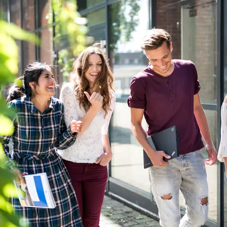 Vier Studierende laufen auf dem Campus in der Sonne und lachen