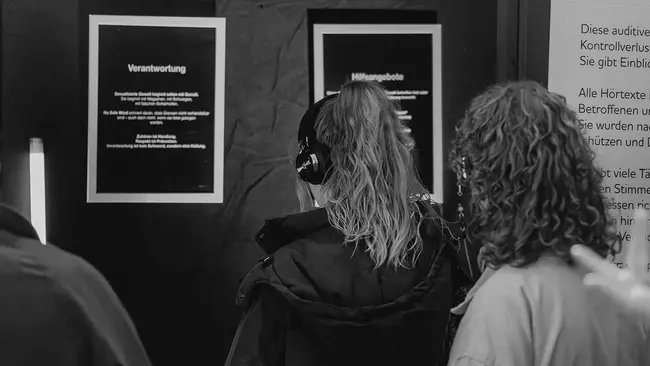 Eine Besucherin der Ausstellung steht vor einer Wand und trägt Kopfhörer
