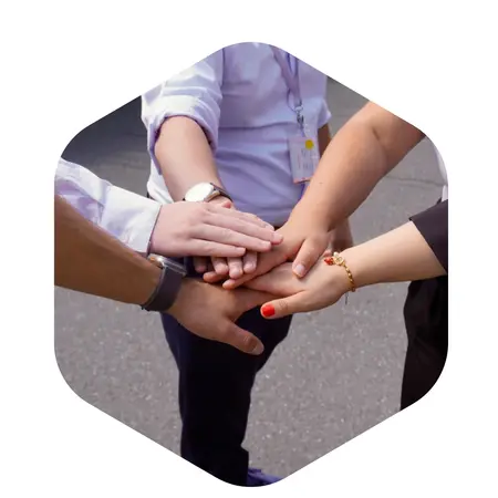 Fünf Hände verschiedener Menschen legen sich übereinander in einer symbolischen Geste der Zusammenarbeit oder Einheit. Die Hände sind teilweise unterschiedlich gekleidet und zeigen eine Vielfalt, die das Teamwork oder Gemeinschaftsgefühl betont.