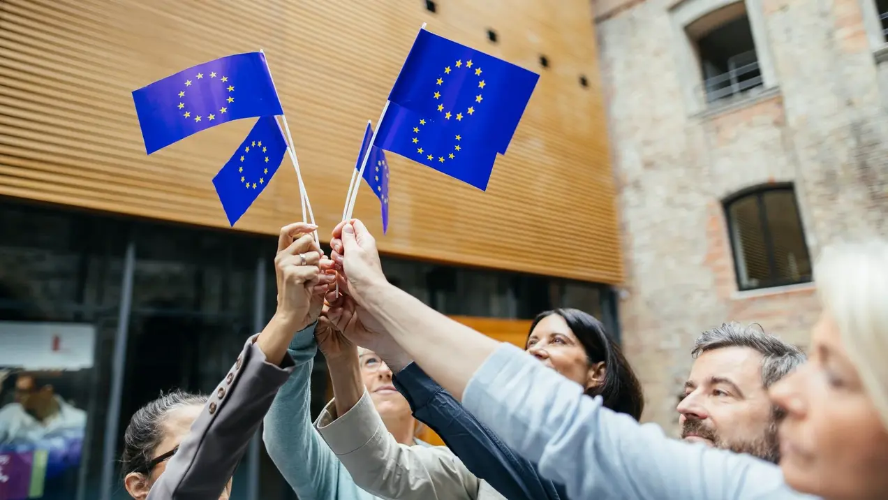 Four EU flags held closely together by four hands