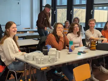 Studierende des Fachbereichs Architektur und Bauingenieurwesen sitzen an Tischen in ihrem Seminarraum und besuchen die Veranstaltung ressourcenschonendes Weihnachten. Auf den Tischen stehen viele Tassen und Getränke.