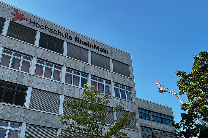 Eine Drehleiter mit zwei Menschen in Dino-Kostümen neben einem Gebäude auf dem Campus Rüsselsheim
