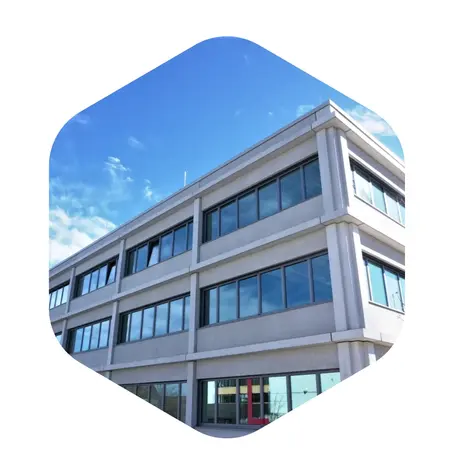 Das Bild zeigt die Fassade eines modernen Bürogebäudes mit mehreren großen Fenstern und einem klaren blauen Himmel im Hintergrund. Die Architektur ist schlicht und funktional gestaltet, mit einer hellgrauen Betonoberfläche.