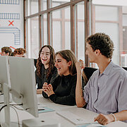Studierende sitzen an Schreibtischen und blicken auf PC-Monitore
