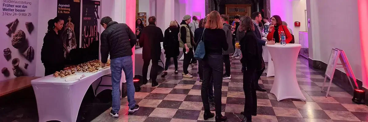 Das Foyer des Museums Wiesbaden erstrahlt in rotem und pinken Licht. An Stehtischen stehen die Besucher:innen mit Getränken und Snacks. 
