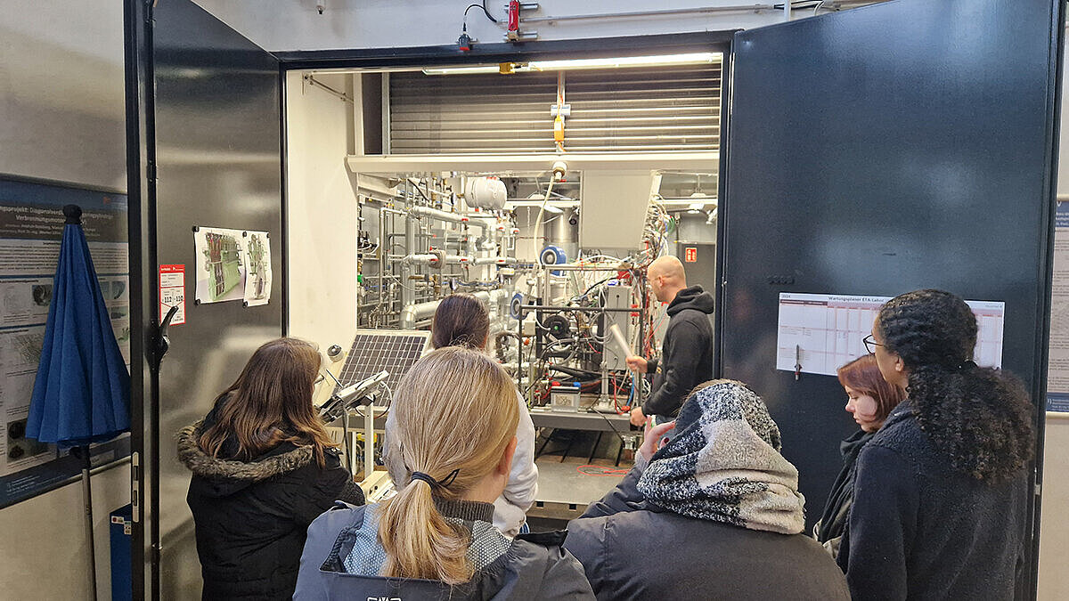 Die Gruppe steht vor der geöffneten Tür eines Prüfstands in der Fahrzeughalle