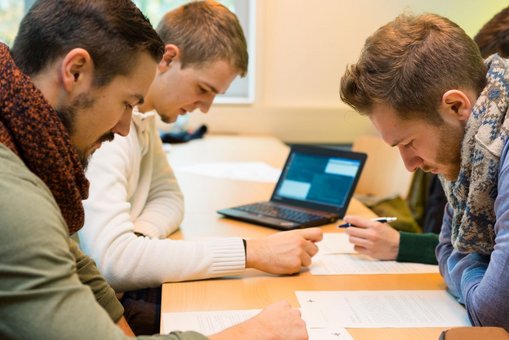 Drei junge Männer sitzen gemeinsam an einem Tisch und lernen