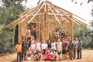 A group of students from HSRM and their hosts from Ghana stand in front of their completed bamboo house.
