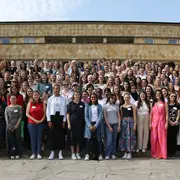 Eine große Gruppe von Frauen steht auf einer Treppe im Freien. Die Teilnehmerinnen tragen verschiedene Kleidung und lächeln in die Kamera. Die Szenarie ist hell und freundlich, umgeben von Pflanzen. Es sind insgesamt mehr als 200 Personen abgebildet.