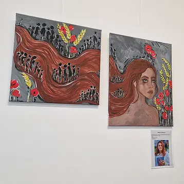 Das Bild zeigt eine Ausstellung mit drei Gemälden an einer Wand. In der Mitte ist ein Porträt einer Frau mit langen, braunen Haaren. Links davon sind Menschenfiguren und rote Blumen dargestellt, und rechts ein weiteres, abstraktes Bild mit verschiedenen Motiven.