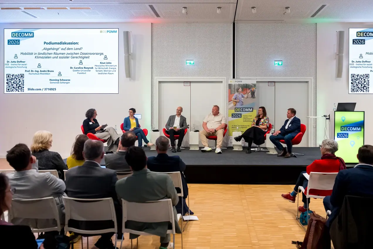 Podiumsdiskussion mit mehreren Gesprächspartner:innen zu den Themen Mobilität in ländlichen Räumen, Daseinsvorsorge und soziale Gerechtigkeit. Auf der Leinwand im Hintergrund sind Details zur Diskussionsrunde, einschließlich eines QR-Codes und Namen der Referent:innen.