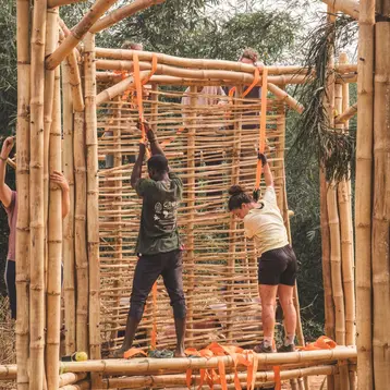 Three people are working together to build a structure out of bamboo. They are using orange ropes to secure the individual elements.