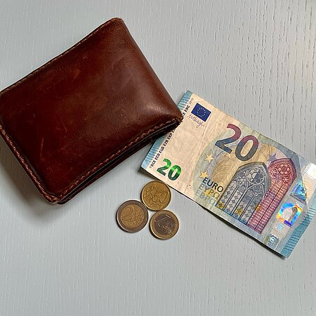Auf einem Tisch liegen Euro-Scheine, Euro-Münzen und ein brauner Geldbeutel aus Leder.