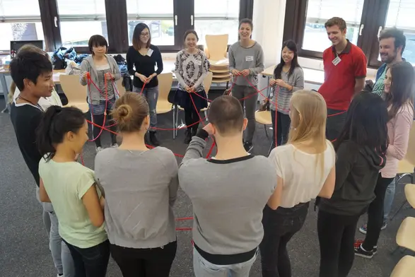 Studierende stehen im Kreis und werfen sich ein Wollknäuel zu, bis ein Spinnennetz entsteht