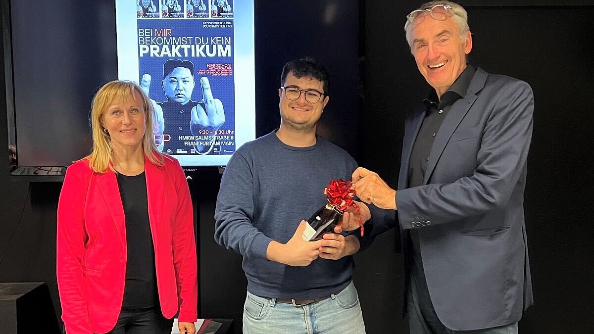 Heike Parakenings (DJV Hessen), Gewinner Maximilian Aurea und Prof. Rüdiger Pichler stehen vor einem Plakat auf dem ein Bild von Kim Jong-un und die Worte "Bei mir bekommst du kein Praktikum" sind