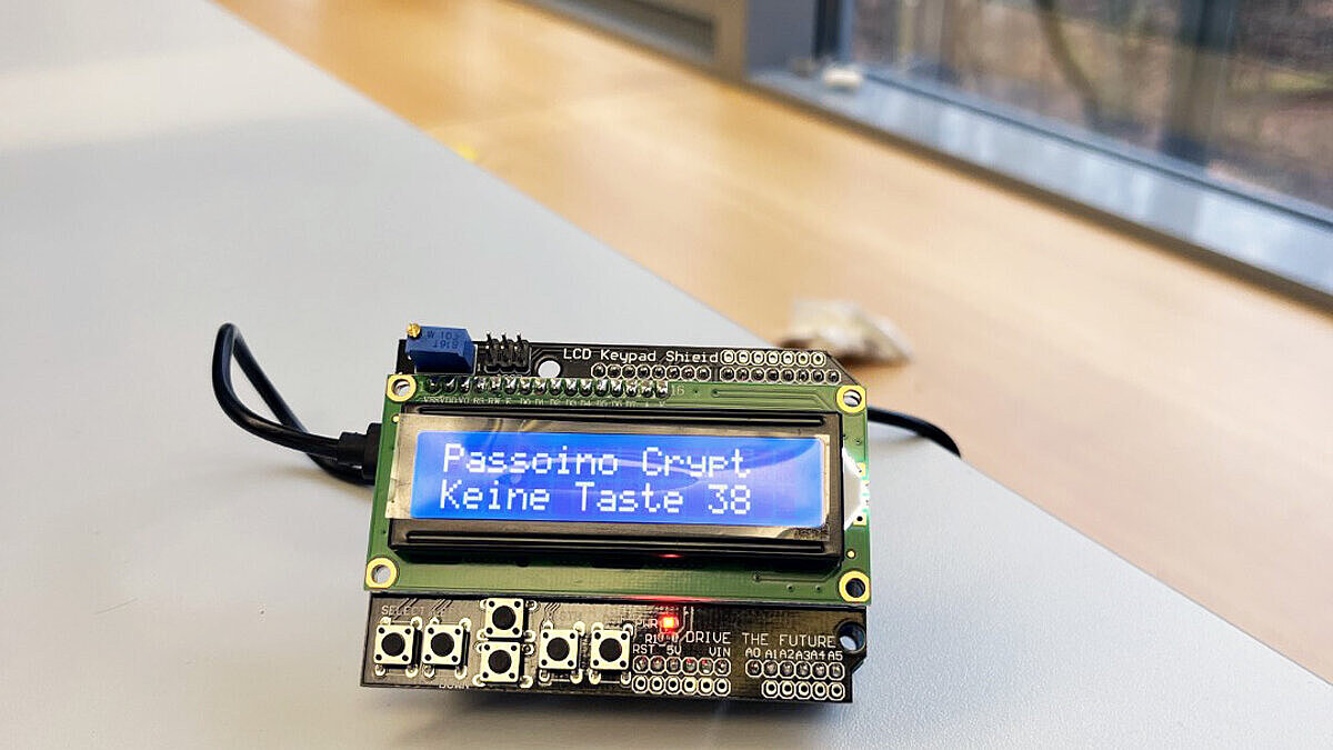 Auf einem Tisch liegt ein elektronisches Gerät, auf dessen Bildschirm zu lesen ist: "Passoino Crypt Keine Taste 38"
