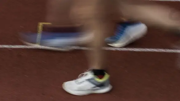 Ein unscharfes Bild von Läufern auf einer Laufbahn. Man sieht die Füße in Sportschuhen, die sich schnell bewegen. Der Hintergrund zeigt die Laufbahn mit weißen Markierungen. Die Bewegung vermittelt Dynamik und Energie des Wettkampfs.