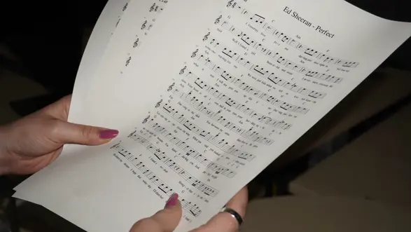 Eine Person hält mehrere Notenseiten des Liedes "Perfect" von Ed Sheeran in den Händen. Die Seiten zeigen eine vollständige Musiknotation mit Noten und Text, die für das Spielen des Liedes notwendig sind.