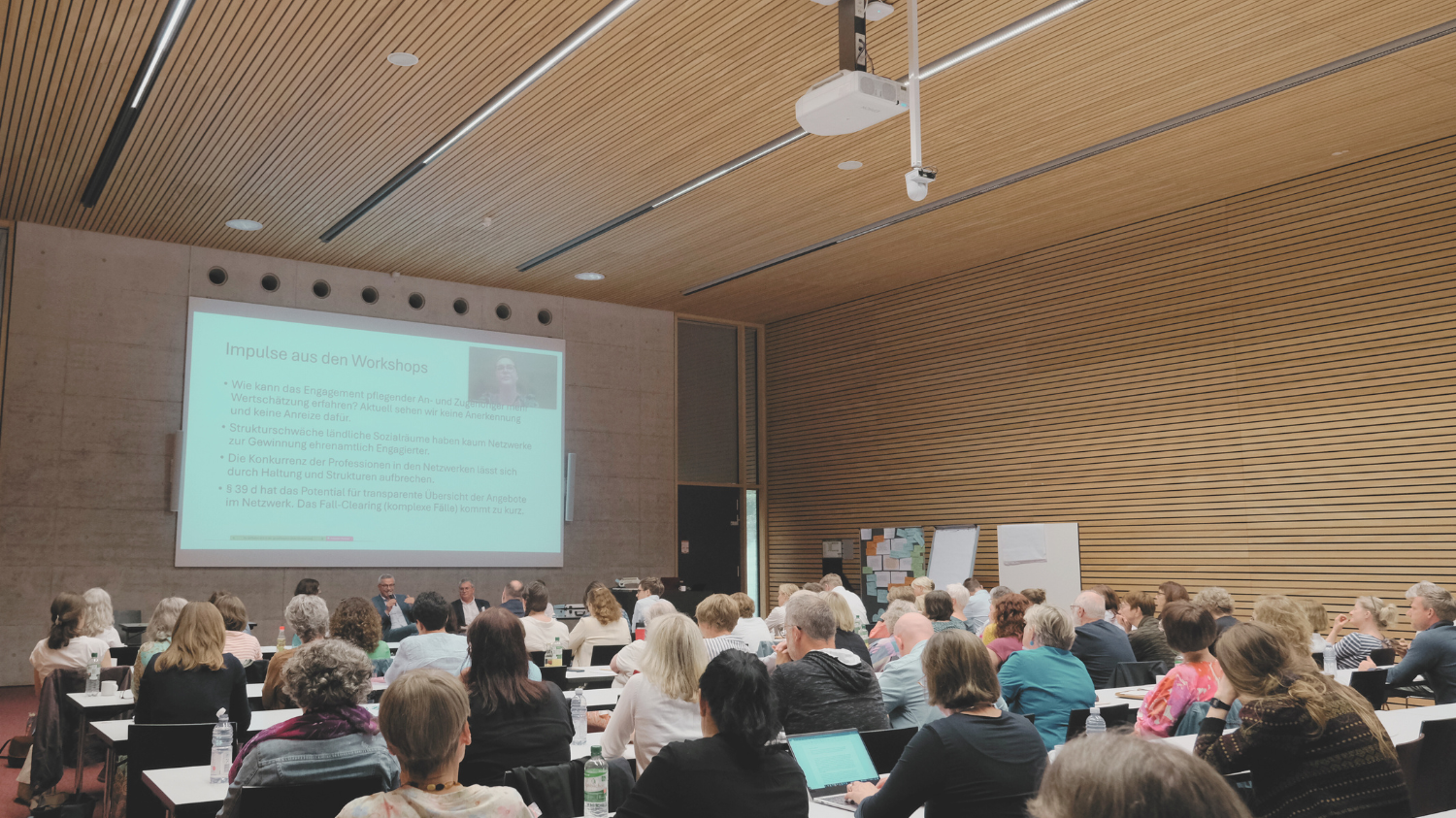 Hörsaal mit Menschen, vorne Podiumsdiskussion