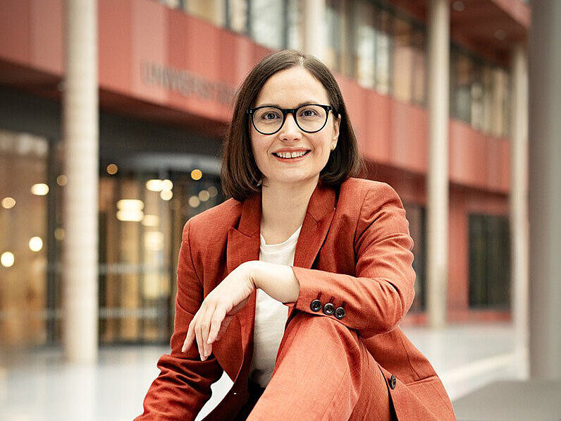 Prof. Dr. Marion Koelle sits on a bench and smiles into the camera