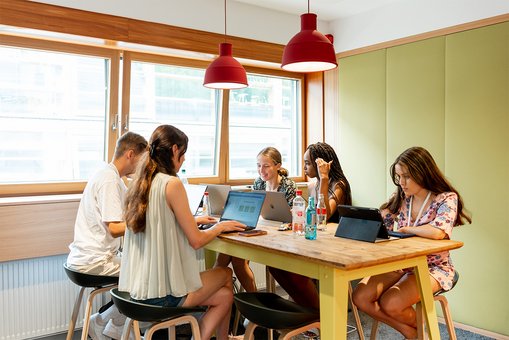 Teilnehmer:innen der Summer School sitzen an einem Tisch und arbeiten an ihren Laptops