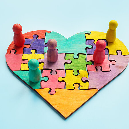Ein Puzzle in Herzform in verschiedenen Farben, auf denen noch ein paar verschiedenfarbige Figuren stehen