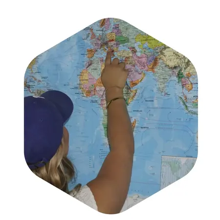Ein Kind mit einem blauen Hut zeigt mit dem Finger auf eine Weltkarte, die geografische Regionen und Länder abbildet. Der Fokus liegt auf der Interaktion mit der Karte.