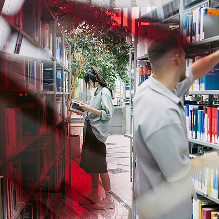 Studierende der Hochschule RheinMain stehen zwischen Regalen in der Bücherei am Campus Unter den Eichen