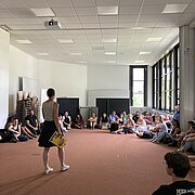 Eine Frau steht vor einer Gruppe Studierender, die vor ihr auf dem Boden sitzt