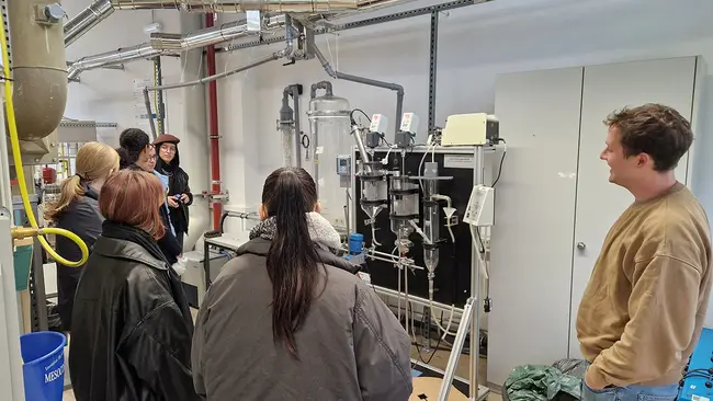 Die Technikantinnen stehen im Halbkreis um eine Laborkläranlage herum