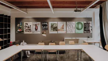 Ansicht von gestellten Stühlen und Tischen vor einer Plakatwand in einem Seminarraum