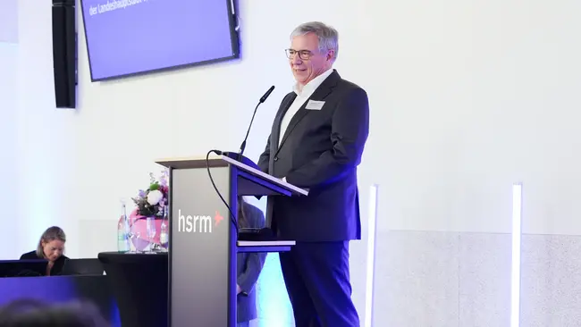 Gert-Uwe Mende in formeller Kleidung steht an einem Rednerpult und hält eine Ansprache. 
